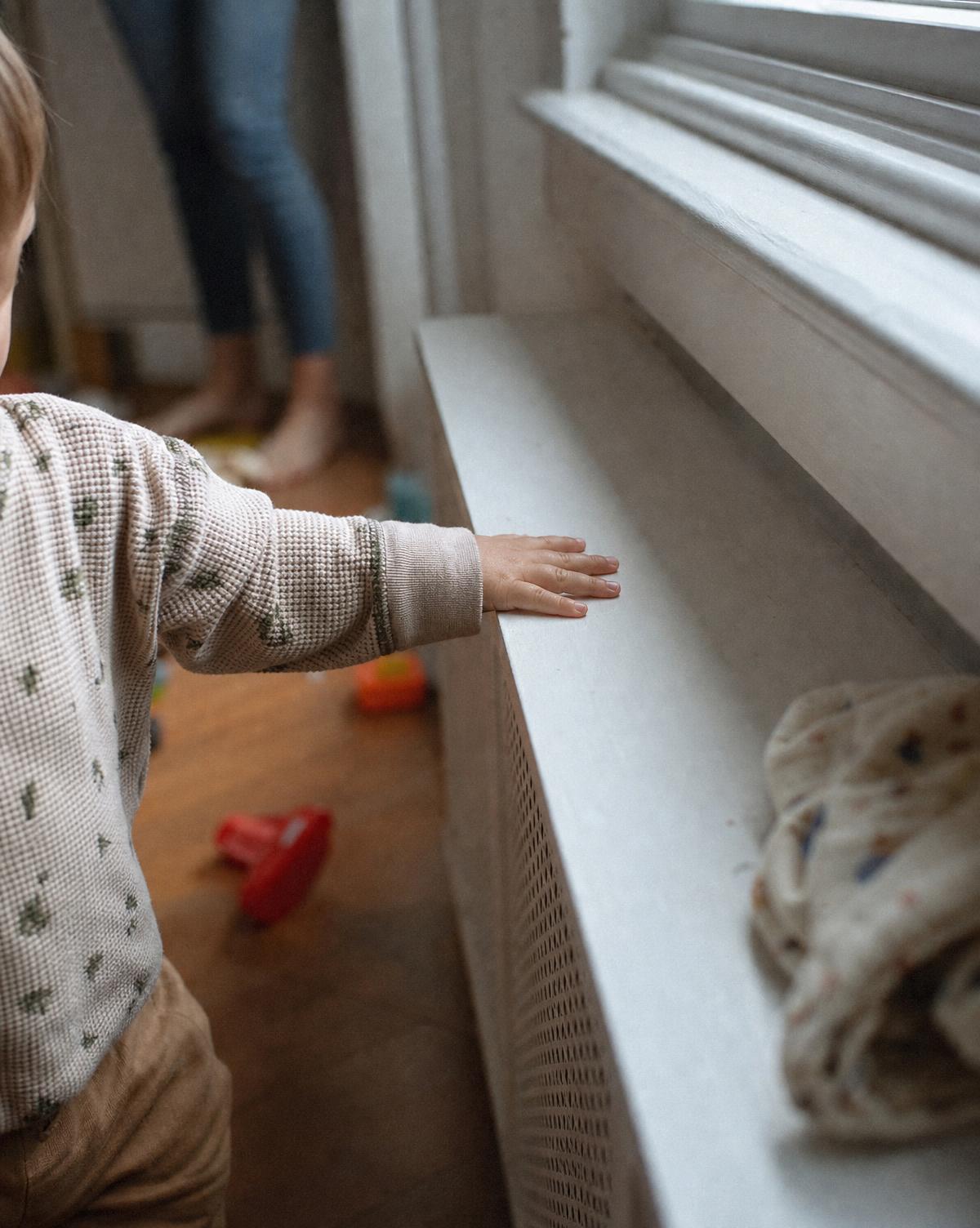 A small child's hand near a covered radiator